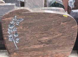 Grabmal aus rötlich gemasertem Naturstein mit Reliefblume